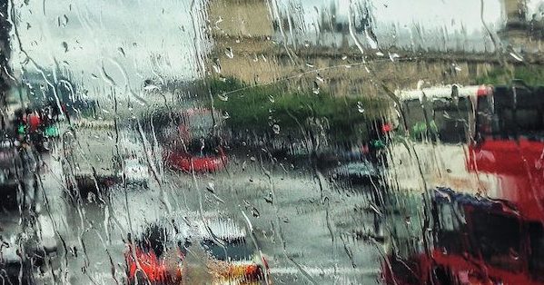 Looking through a wet window at a scene of London in the rain, with cars on the road in the foreground